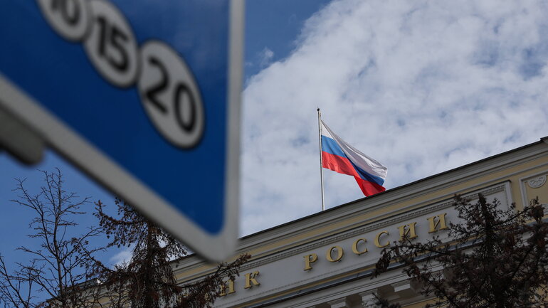 The lettering ‘Банк России’ (Bank of Russia) can be seen in the upper part of the neoclassical façade of the Russian Central Bank. The Russian national flag flutters above it.