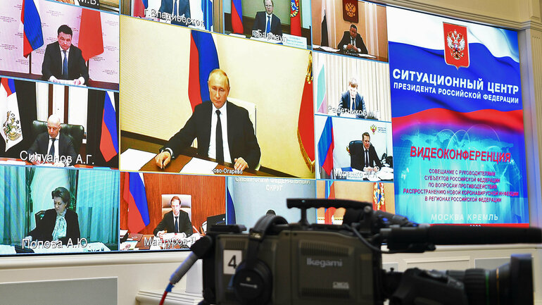 A digital video conference is taking place on a screen. Vladimir Putin, other politicians in suits and the Russian flag can be seen on the participants' screens.
